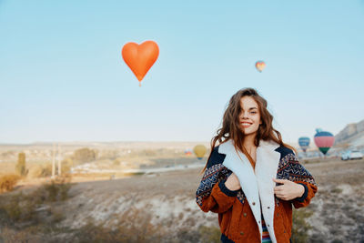 Portrait of young woman with balloons against sky