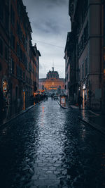 Wet cobblestones road amidst buildings in city