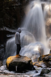 Man standing on rock by blurred motion of waterfall