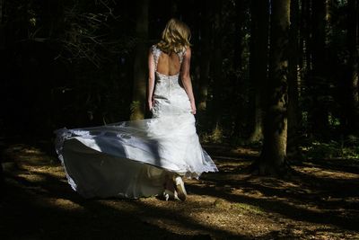 Rear view full length of bride standing by trees at forest