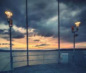 Illuminated street light by sea against sky during sunset