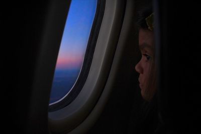 Close-up of girl looking through airplane window at sunset
