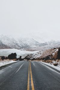 Road by snowcapped mountains against sky during winter