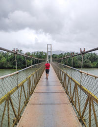 Rear view of woman walking on footbridge against sky