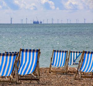 Deck chairs on beach against sky