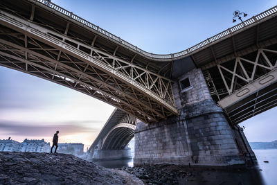 Man standing below bridge during sunset