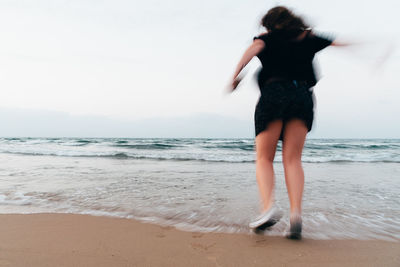Rear view of woman on beach against sky