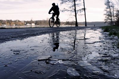 Low angle view of person riding bicycle on street by frozen puddle