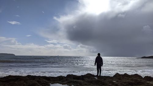 Rear view of man standing at beach against sky