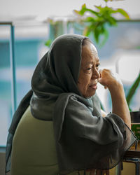 Senior malaysian muslim woman stay at home. sitting at the balcony apartment while having breakfast.