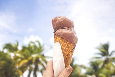 Close-up of hand holding ice cream against sky