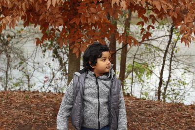 Thoughtful boy standing against autumn trees