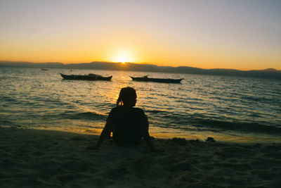 Rear view of silhouette man sitting on beach during sunset