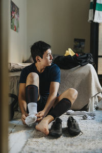 Teenage boy wearing sock while sitting on ground at home