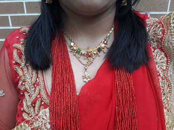 Midsection of woman wearing necklace standing against brick wall