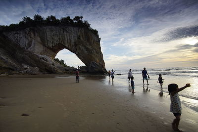 People on rocks at beach against sky