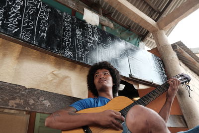 Low angle view of man playing guitar against blackboard