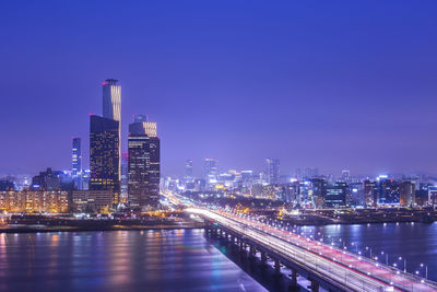 Illuminated buildings by river against sky in city at night