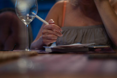 Midsection of woman holding glass while sitting on table