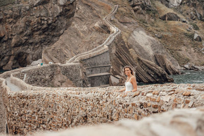 Portrait of young woman standing by stone wall