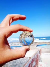 Close-up of hand holding sea against clear blue sky