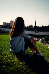 Rear view of woman sitting on grass against sky