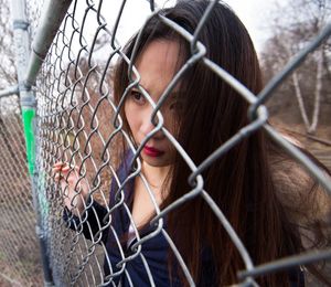 Close-up of young woman looking through chainlink fence