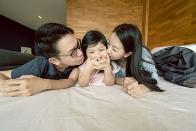 Mother and father kissing daughter on bed at home