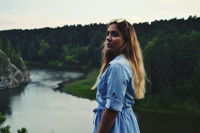 Portrait of young woman standing against river in forest