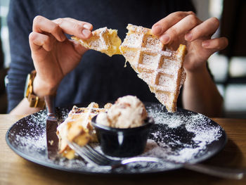 Anonymous person breaking off piece of soft waffle over plate with tasty ice cream while sitting at table in restaurant person