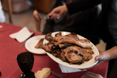 Unrecognizable woman is serving the barbecue meat on the table with red tablecloth. close up.