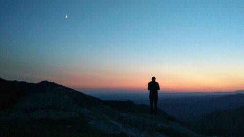 Silhouette man standing on rock against sky during sunset