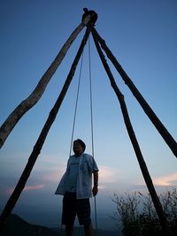 Man standing by wooden structure on cliff against sky during sunset