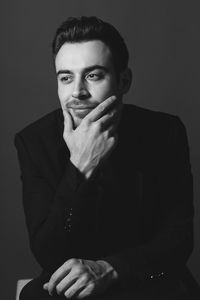 Portrait of young man sitting against gray background