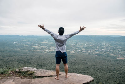 Rear view of man with arms outstretched standing on hum hod cliff against sky