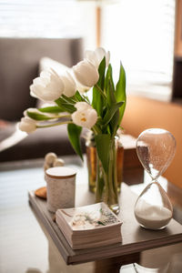 Close-up of flowers in vase with picture frames and hourglass on table at home
