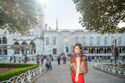 Portrait of smiling woman standing on footpath in city