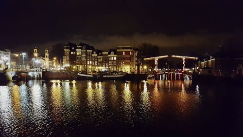 Illuminated city by river against sky at night