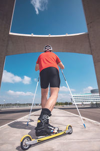 Rear view of man with ski roller on road against sky