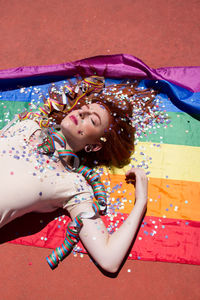 High angle view of young woman lying with confetti on rainbow flag