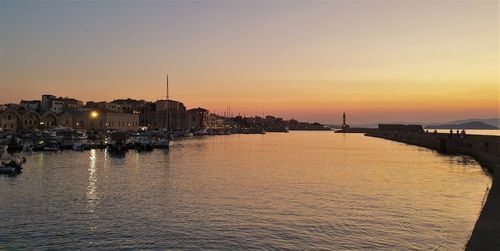 Sea by illuminated buildings against sky during sunset