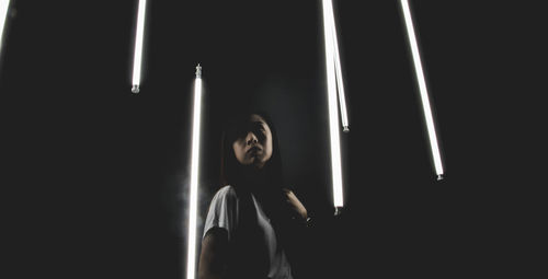 Young woman standing amidst illuminated fluorescent lights at night