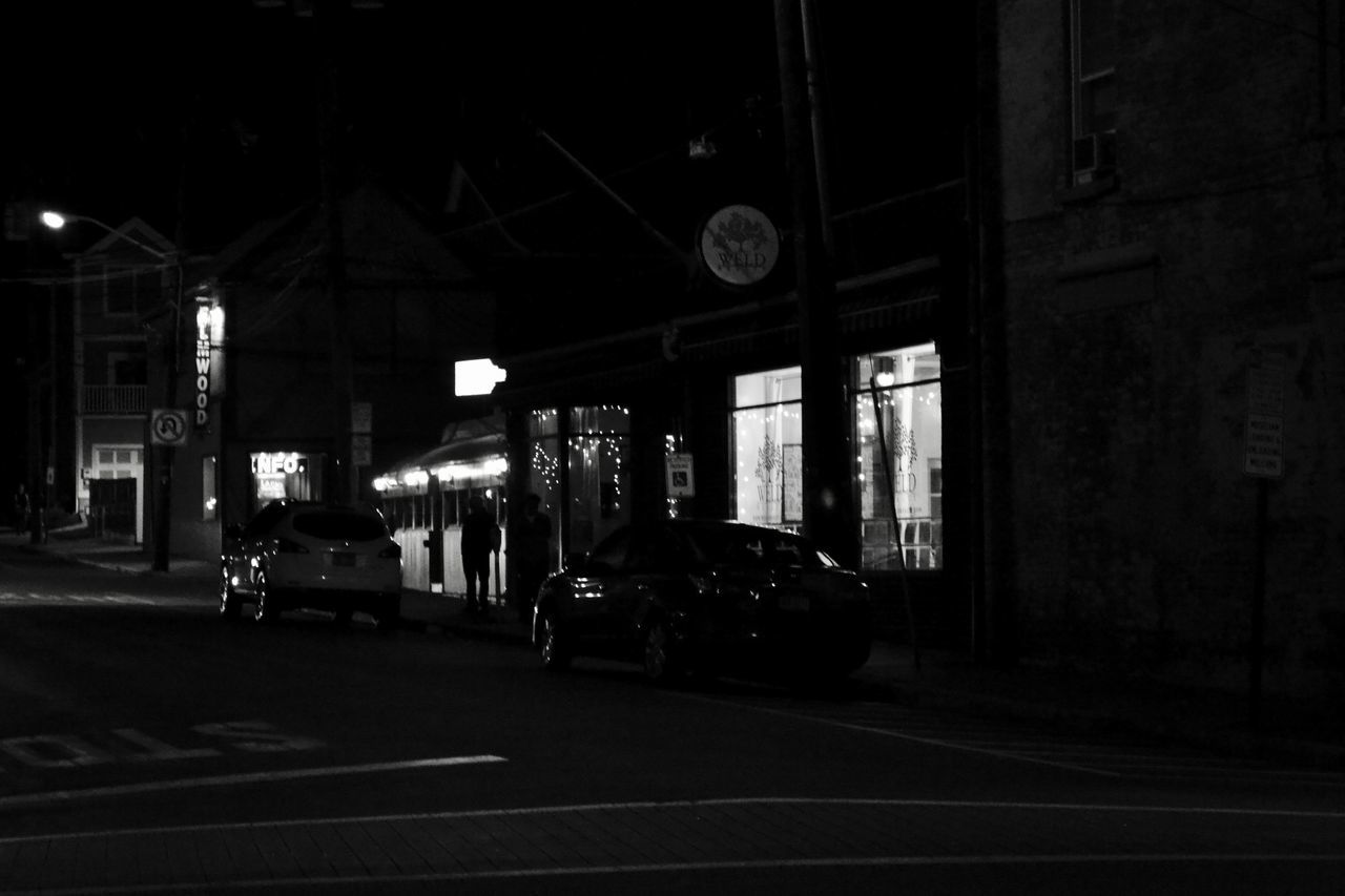 CARS ON ROAD BY ILLUMINATED STREET AT NIGHT