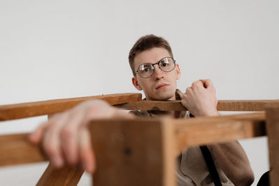Portrait of young man sitting with ladder against white background