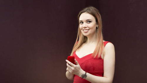 Portrait of smiling young woman standing against red background