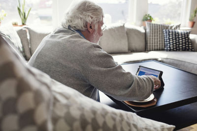 Senior man using digital tablet while sitting on sofa at home