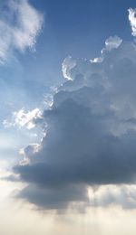 Low angle view of sunlight streaming through clouds