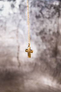 Close-up of chain with cross pendant hanging against wall