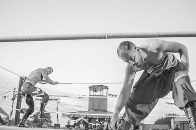 Side view of a shirtless man with arms raised against clear sky