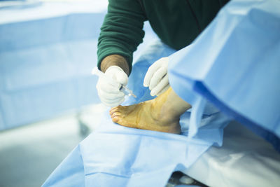 Midsection of doctor injecting syringe on patient leg at hospital